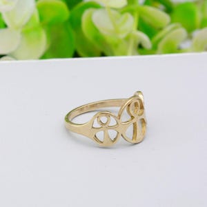 May include: A gold-colored ring with an openwork design featuring a series of connected shapes. The ring has a smooth, polished finish and is set against a white background. The ring's design is symmetrical and geometric.