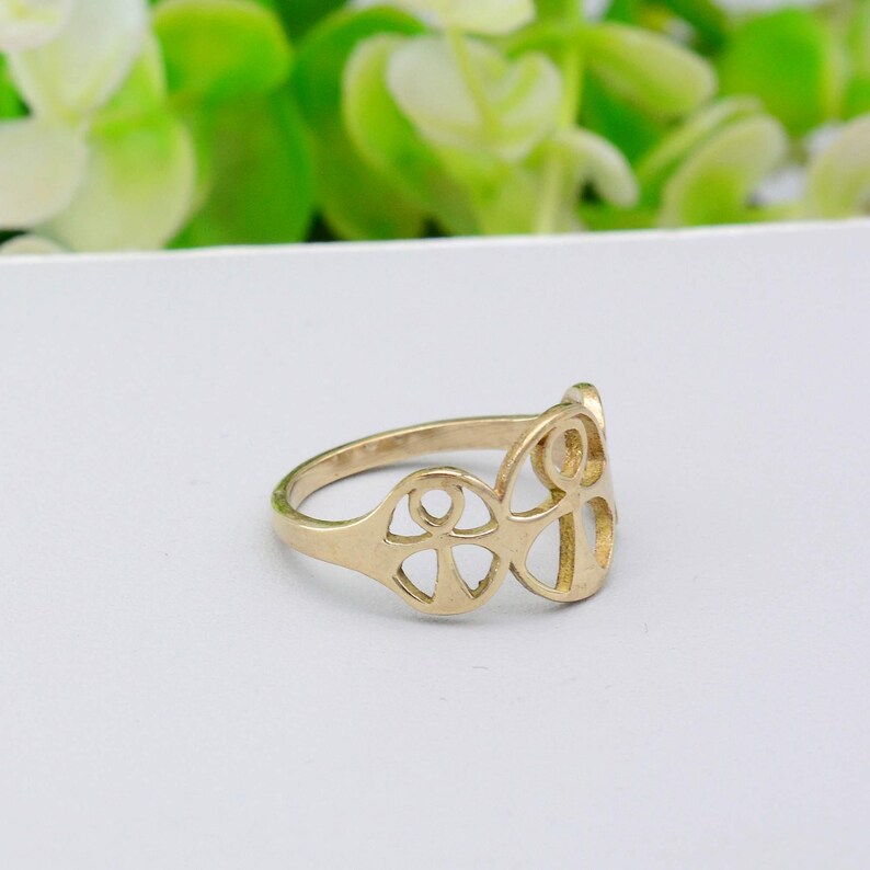 May include: A gold-colored ring with an openwork design featuring a series of connected shapes. The ring has a smooth, polished finish and is set against a white background. The ring's design is symmetrical and geometric.