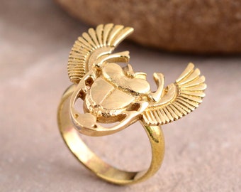 May include: A gold ring featuring a scarab beetle design. The beetle has wings and is intricately carved.