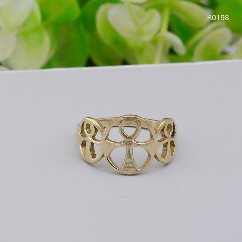 May include: A gold-colored ring with an openwork design featuring an Ankh symbol in the center and stylized shapes on either side. The ring is set against a light background, with the product code "R0198" visible.