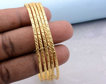 May include: A set of six gold-toned bangles with a textured design. The bangles are stacked on top of each other.