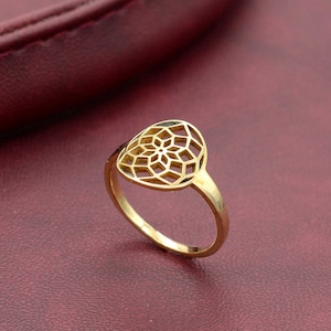 May include: Gold ring with a delicate, intricate, circular design. The ring is made of a single piece of metal and has a smooth, polished finish.
