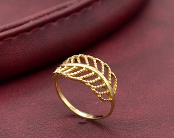 May include: A gold leaf-shaped ring with a delicate, intricate design. The ring is made of a thin metal and has a simple band.