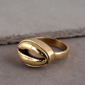 Pode incluir: Um anel dourado com um design de concha. O anel é feito de metal e tem um acabamento liso.
