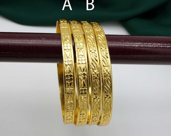 Könnte beinhalten: Satz von vier goldfarbenen Armreifen mit aufwendigen floralen und geometrischen Mustern. Die Armreifen sind auf einer braunen Oberfläche gestapelt.