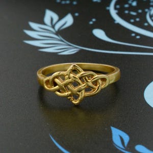 May include: A gold ring featuring a Celtic knot design. The knot is intricate and detailed, and the ring has a polished finish.
