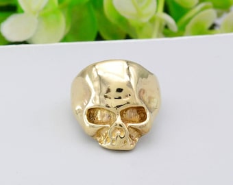 May include: A gold skull ring with a detailed design. The ring is made of metal and has a smooth finish.
