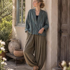 Könnte beinhalten: Eine dunkelgrüne Knopfjacke mit langen Ärmeln und zwei Vordertaschen, kombiniert mit einer locker sitzenden olivgrünen Pluderhose. Die Jacke hat einen strukturierten Stoff und einen V-Ausschnitt, während die Hose eine geraffte, voluminöse Form aufweist.