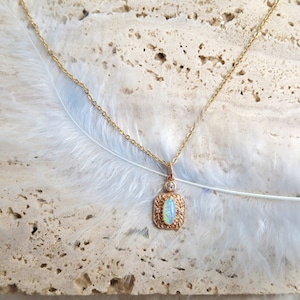 May include: A delicate gold chain necklace with a pendant featuring a light blue oval opal surrounded by a gold filigree design and small clear gemstones.