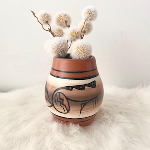 May include: A terracotta vase with a geometric design in brown and white. The vase is filled with dried white flowers.