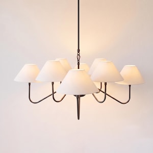 May include: A multi-arm chandelier featuring a dark brown metal frame with eight curved arms, each supporting a white conical fabric lampshade. The fixture is suspended by a central rod and emits a soft, warm glow from the illuminated shades.