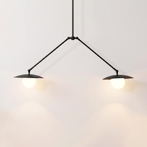 May include: A modern black metal pendant light fixture with two lamps. Each lamp has a round, white light bulb and a circular, flat shade. The fixture is suspended from the ceiling by a single rod and two angled arms.