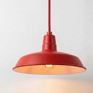 Może przedstawiać: Jasnoczerwona metalowa lampa wisząca z szerokim kloszem w kształcie kopuły i pasującym czerwonym przewodem. Wnętrze klosza ma jasnokremowy kolor, a w środku oprawy widoczna jest pojedyncza świecąca żarówka.