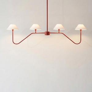 May include: A linear chandelier featuring a matte terracotta-colored metal frame with four upward-curving arms. Each arm supports a small, conical white lampshade. The fixture is suspended by a single central rod extending from the top center.