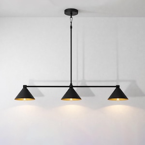 Puede incluir: Una lámpara colgante negra de tres luces. La lámpara tiene tres pantallas en forma de cono con interiores dorados, suspendidas de una varilla negra. La luz está montada en el techo con una placa circular.