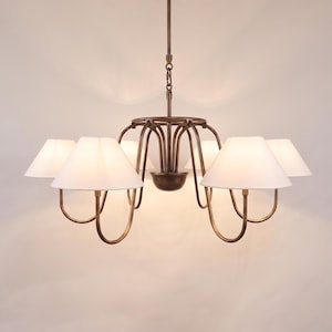 May include: A bronze-colored chandelier with six white lampshades. The light fixture has a central bowl and curved arms supporting the shades. The design is elegant and suitable for a dining room or living room.