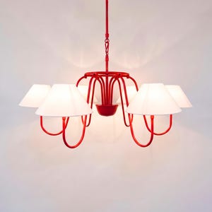 May include: Red chandelier with five white lampshades. The fixture has a central bowl and curved arms supporting the shades. The design is modern and minimalist, suitable for interior lighting.