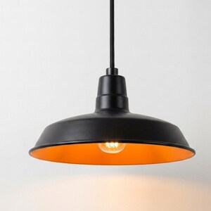 May include: A matte black pendant light fixture with a wide, bowl-shaped shade. The interior of the shade features a vibrant orange finish, and a single glowing light bulb is visible in the center, suspended by a thin black cord.
