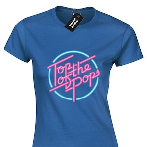 May include: A royal blue t-shirt with the words "Top of the Pops" in a pink neon font, set within a light blue circle. The shirt has a crew neck and short sleeves. A black tag with white text is attached to the shirt.