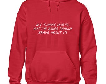 May include: A bright red hoodie with a front pocket and a drawstring hood. The white text on the front reads: "MY TUMMY HURTS, BUT I'M BEING REALLY BRAVE ABOUT IT!" A casual, comfortable garment.