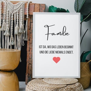 Może przedstawiać: Biały wydruk w ramie z tekstem "Familie ist da, wo das Leben beginnt und die Liebe niemals endet." z różowym sercem pod tekstem. Wydruk leży na plecionym pufie ze słomy przed ceglanym kominkiem.