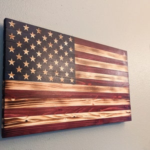 May include: A wooden American flag with red, white, and blue stripes and a field of blue with white stars. The flag is mounted on a wall.