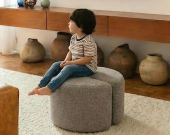 Könnte beinhalten: Modernes Wohnzimmer mit einem an der Wand befestigten Fernseher über einer Holzkonsolentisch. Dekorative Vasen und Töpferwaren sind ausgestellt, zusammen mit einem Kind, das auf einem grauen Hocker sitzt. Ein geflochtener Korb und Bücher befinden sich auf einem Regal darüber.