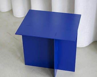 Op de afbeelding: Een helderblauwe, geometrische bijzettafel. De tafel is gemaakt van gevouwen metalen platen, waardoor een doosvorm ontstaat met een platte bovenkant. Het ontwerp heeft een kruisvormige basis voor stabiliteit. Geschikt voor binnengebruik.