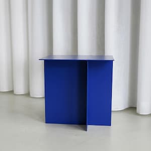 May include: A modern, cobalt blue side table with a minimalist design. The table has a rectangular top and a solid, geometric base. The table is made of a solid material and is suitable for various interior design styles.