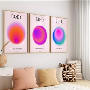 Op de afbeelding: Drie ingelijste prints met roze achtergronden en kleurrijke gradiëntcirkels. De bovenkant van elke print heeft de woorden "BODY", "MIND" en "SOUL" in zwarte tekst. Onder de cirkels heeft elke print een zin in zwarte tekst: "I care for my body", "I think positively" en "I radiate love".