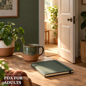May include: A dark green notebook with an elastic closure sits on a wooden table next to a two-toned green and brown ceramic mug. The text on the image reads FORGEBLOOM PDA TOOLS PDA FOR ADULTS Autonomy-First Tools for Demand Avoidance.