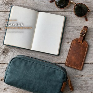 May include: An open notebook with blank pages featuring the text TRAVEL & ROUTINE DISRUPTION, a dark teal zippered pouch, a brown leather luggage tag with a metal buckle, and tortoise shell sunglasses with dark lenses.