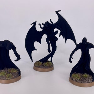 May include: Three black painted miniature figures, one with wings, standing on brown bases with green grass.