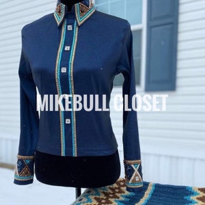May include: A navy blue long-sleeved shirt with decorative embellishments. The shirt features a high collar and cuffs with brown, gold, and turquoise accents. The front has a vertical turquoise and gold trim with square silver buttons. The text "MIKEBULL CLOSET" is across the front.