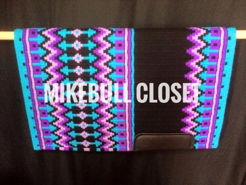 May include: A black and turquoise saddle pad with a purple and pink geometric pattern. The saddle pad has a black leather flap with the text "MIKEBULL CLOSET" printed on it.