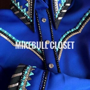 Könnte beinhalten: Ein langärmliges Hemd in Königsblau mit schwarzen, silbernen und türkisfarbenen Verzierungen. Das Hemd hat einen spitzen Kragen und einen Knopfleisten vorne. Der Text "MIKEBULL CLOSET" ist auf dem Hemd sichtbar.