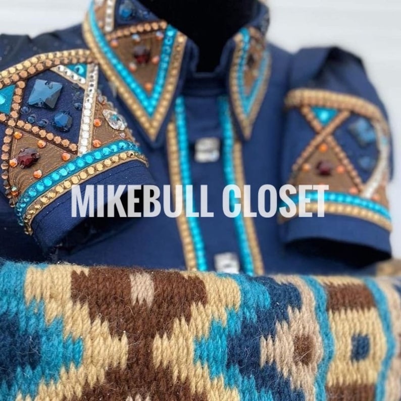 May include: A navy blue show shirt with intricate embellishments. The shirt features turquoise, brown, and gold accents, with sparkling gemstones and detailed patterns on the collar and sleeves. The text "MIKEBULL CLOSET" is visible.