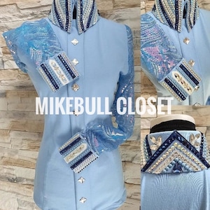 May include: A light blue button-up shirt with a sequined collar and cuffs. The collar and cuffs have a white and blue design with rhinestones. The shirt has a Mikebull Closet logo on the front.