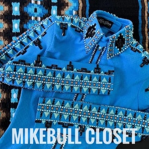 Op de afbeelding: Een blauw denim jack met een zwart en turquoise geometrisch patroon en strass. Het jack heeft een kraag en een knoopsluiting. De tekst "MIKEBULL CLOSET" is zichtbaar onderaan de afbeelding.