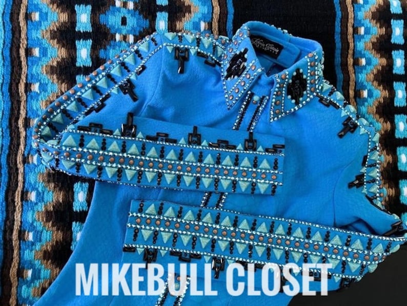 Op de afbeelding: Een blauw denim jack met een zwart en turquoise geometrisch patroon en strass. Het jack heeft een kraag en een knoopsluiting. De tekst "MIKEBULL CLOSET" is zichtbaar onderaan de afbeelding.