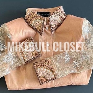 Puede incluir: Una camisa de botones marrón claro con una superposición de encaje en las mangas. El cuello y los puños están adornados con diamantes de imitación y detalles marrones. La camisa tiene el texto "Mike Bull Closet" impreso en la parte delantera.
