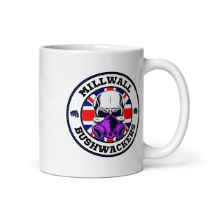 Puede incluir: Taza de cerámica blanca con un logotipo en blanco y negro que presenta una calavera con una máscara de gas morada. El logotipo está rodeado por un círculo azul con el texto "Millwall Bushwackers" en blanco. El logotipo también incluye una bandera de la Unión Jack roja, blanca y azul.