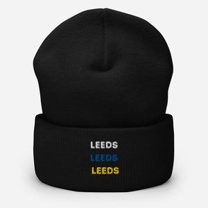Puede incluir: Gorro negro con un "LEEDS" bordado en blanco, azul y amarillo en el puño.