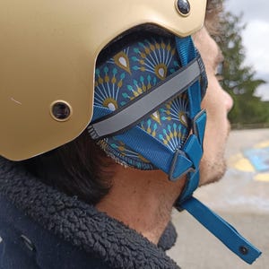 Pode incluir: Capacete dourado com forro interior azul e estampado. O capacete tem uma correia azul com uma faixa refletora. Projetado para segurança e proteção.