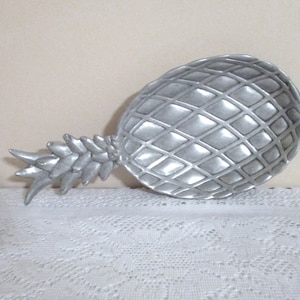 May include: A silver pineapple-shaped dish with a textured surface. The dish is made of metal and has a realistic pineapple design.