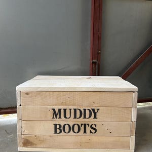 May include: A wooden storage box with the words "Muddy Boots" printed on the front. The box is made of natural wood and has a rustic look.