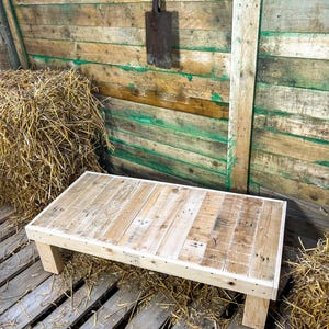 May include: A rustic wooden coffee table made from reclaimed pallet wood. The table has a natural wood finish and is sitting on a pallet floor with straw bales in the background.