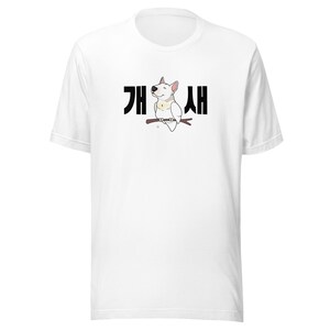 May include: White t-shirt with a cartoon white bull terrier sitting on a branch with the Korean text "개새" printed in black.