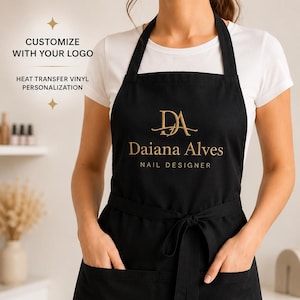 May include: A black apron featuring a gold heat transfer vinyl logo that reads DA Daiana Alves NAIL DESIGNER. The apron includes a neck strap, a waist tie, and two front pockets. Text on the image reads CUSTOMIZE WITH YOUR LOGO and HEAT TRANSFER VINYL PERSONALIZATION.