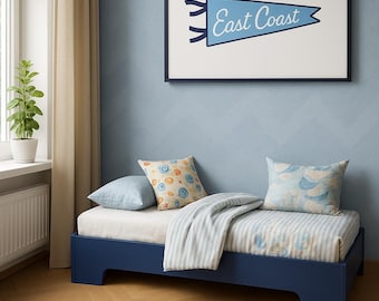 May include: A navy blue twin bed with a white and blue striped comforter and patterned pillows. A framed pennant with "East Coast" text hangs above the bed. A round, cream-colored rug sits on the floor.
